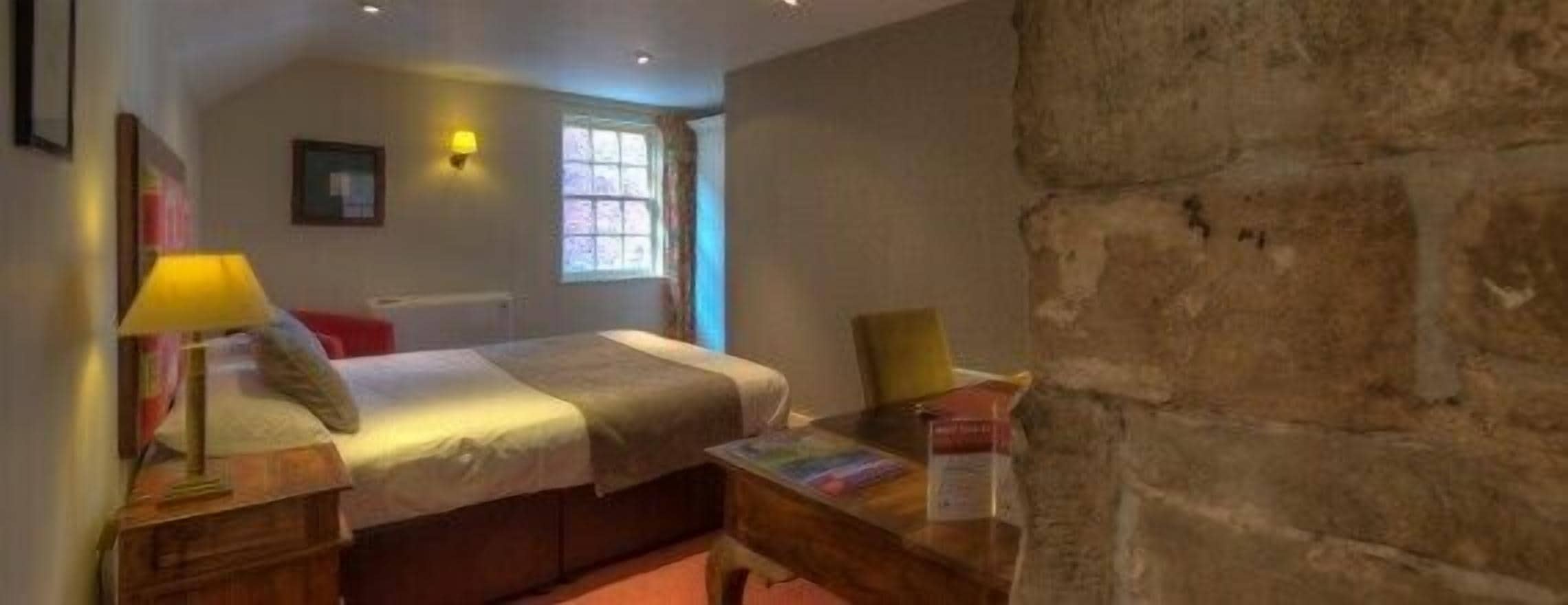 A bedroom with a bed, bedside tables, a window, and a stone wall.