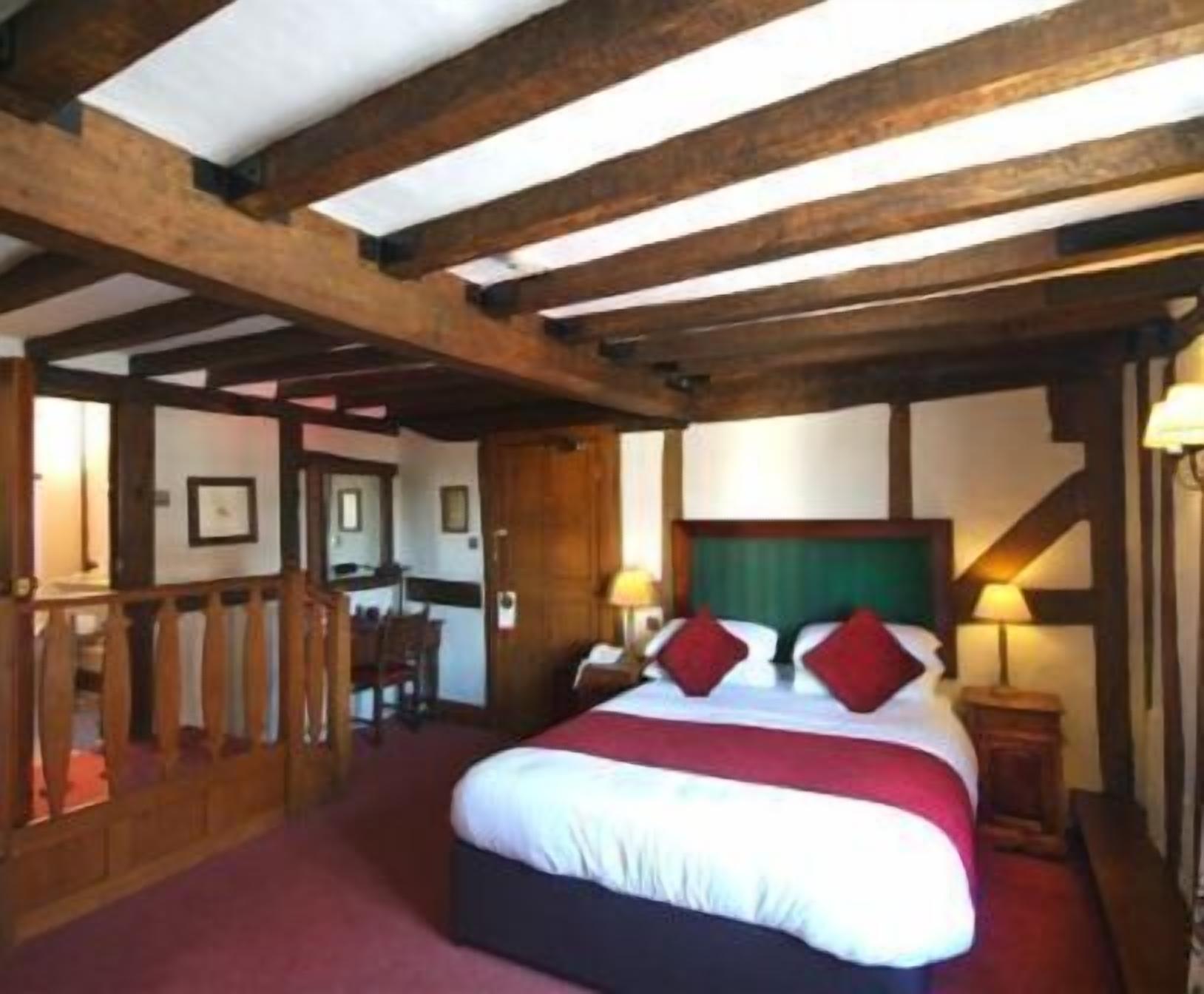 A room with a wooden ceiling, a bed with white and red bedding, and a desk with a chair.