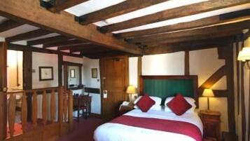 A room with a wooden ceiling, a bed with white and red bedding, and a desk with a chair.