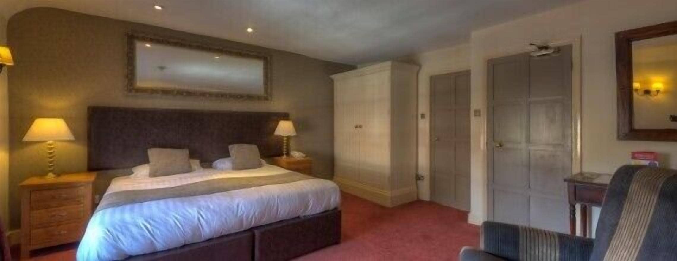 A hotel room with a large bed, two bedside tables with lamps, a chair, and a wardrobe.