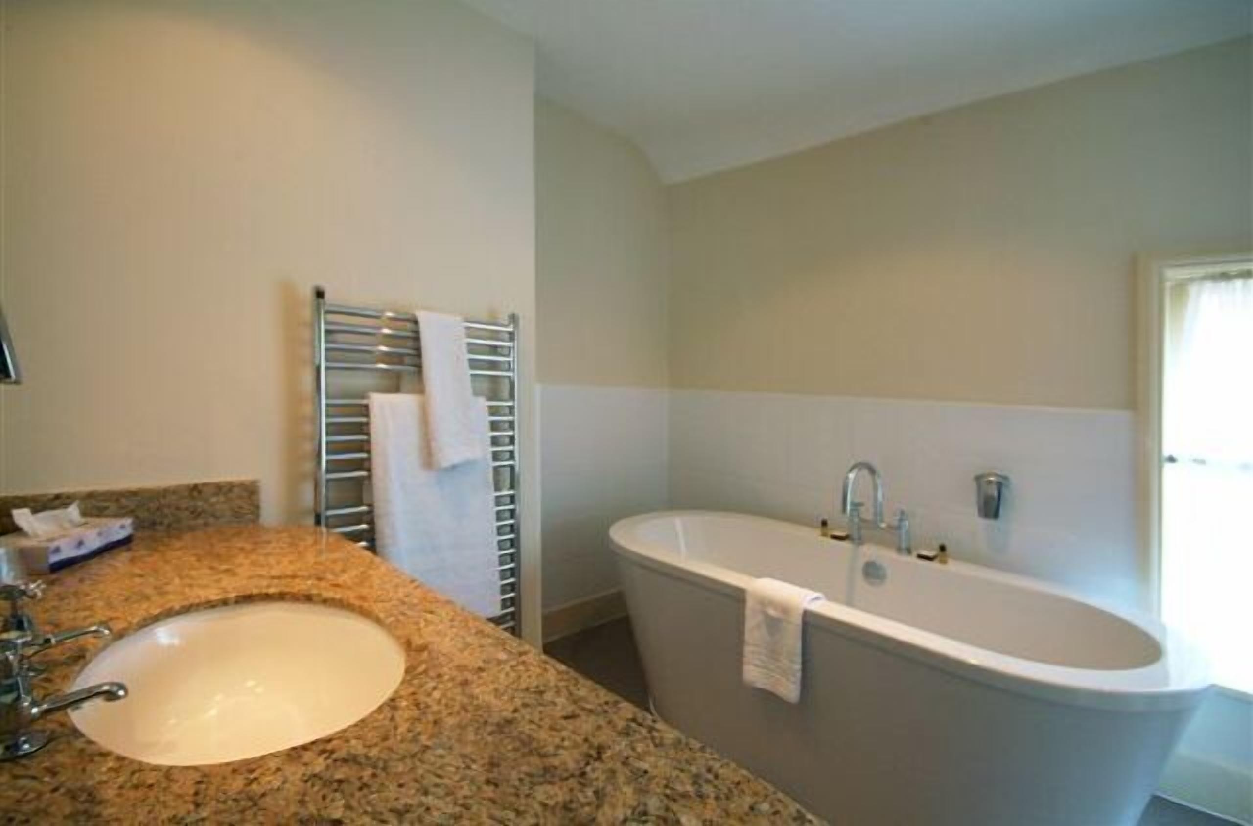 Un baño con lavamanos de encimera de granito, una bañera independiente y un perchero para toallas.