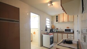 A compact kitchen with a refrigerator, microwave, oven, and a small dining table. - Ribeiro 704 (Rio de Janeiro)