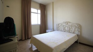 A bedroom with a bed, a desk with a fan, a window with curtains, and a nightstand. - Ribeiro 704 (Rio de Janeiro)
