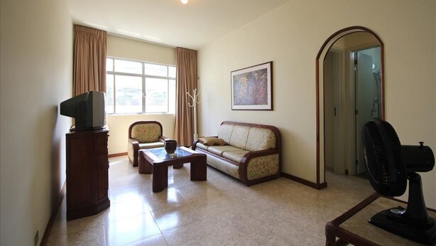 A living room with a sofa, a coffee table, a TV on a stand, a fan, and a window with curtains. - Ribeiro 704 (Rio de Janeiro)