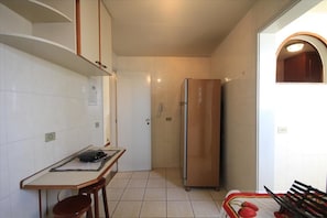 Cozinha compacta com paredes azulejadas brancas, geladeira de aço inoxidável, mesa de jantar com dois banquinhos e uma pequena janela com arco.