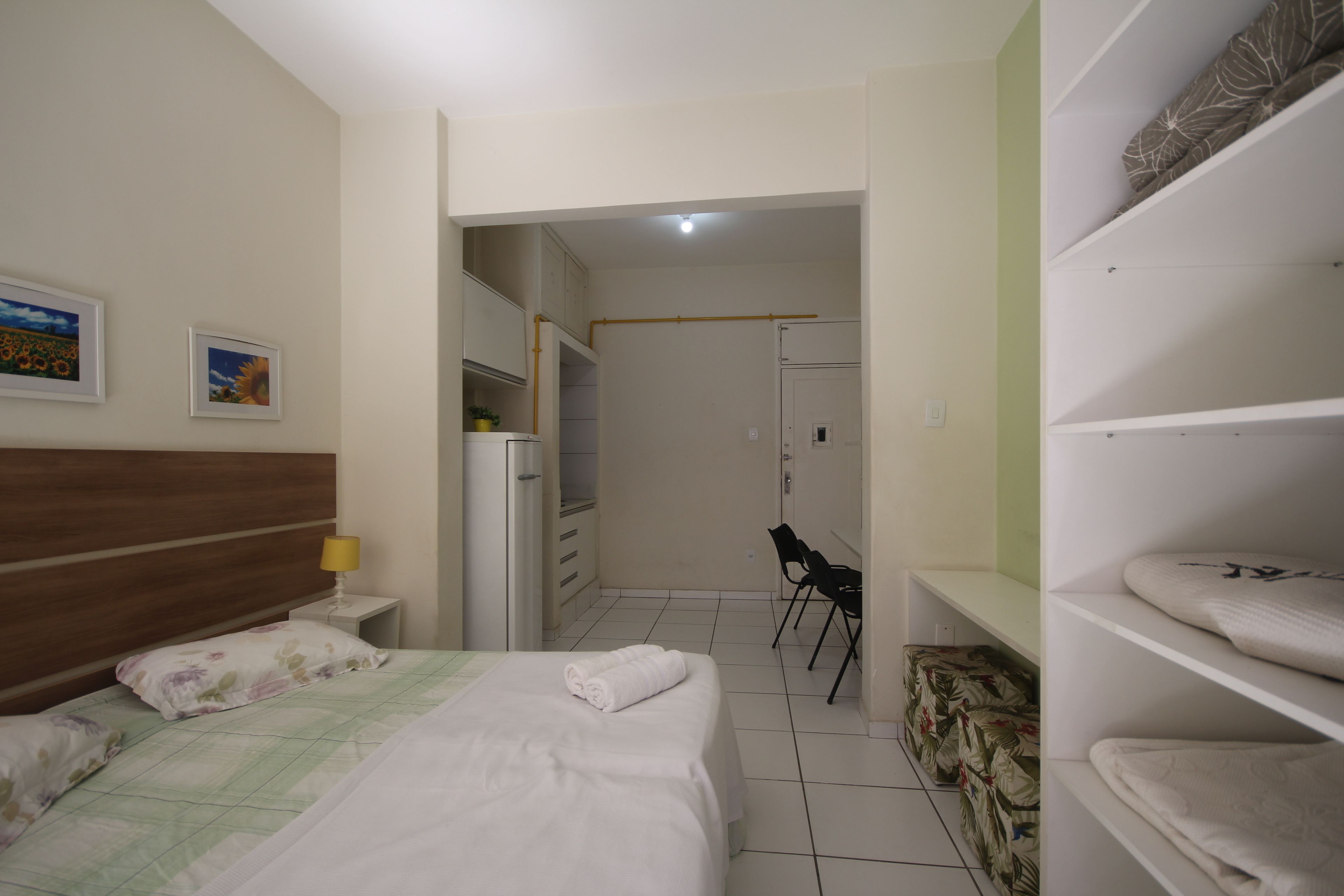 Una habitación de hotel con cama, sillón, armario y escritorio con lámpara.