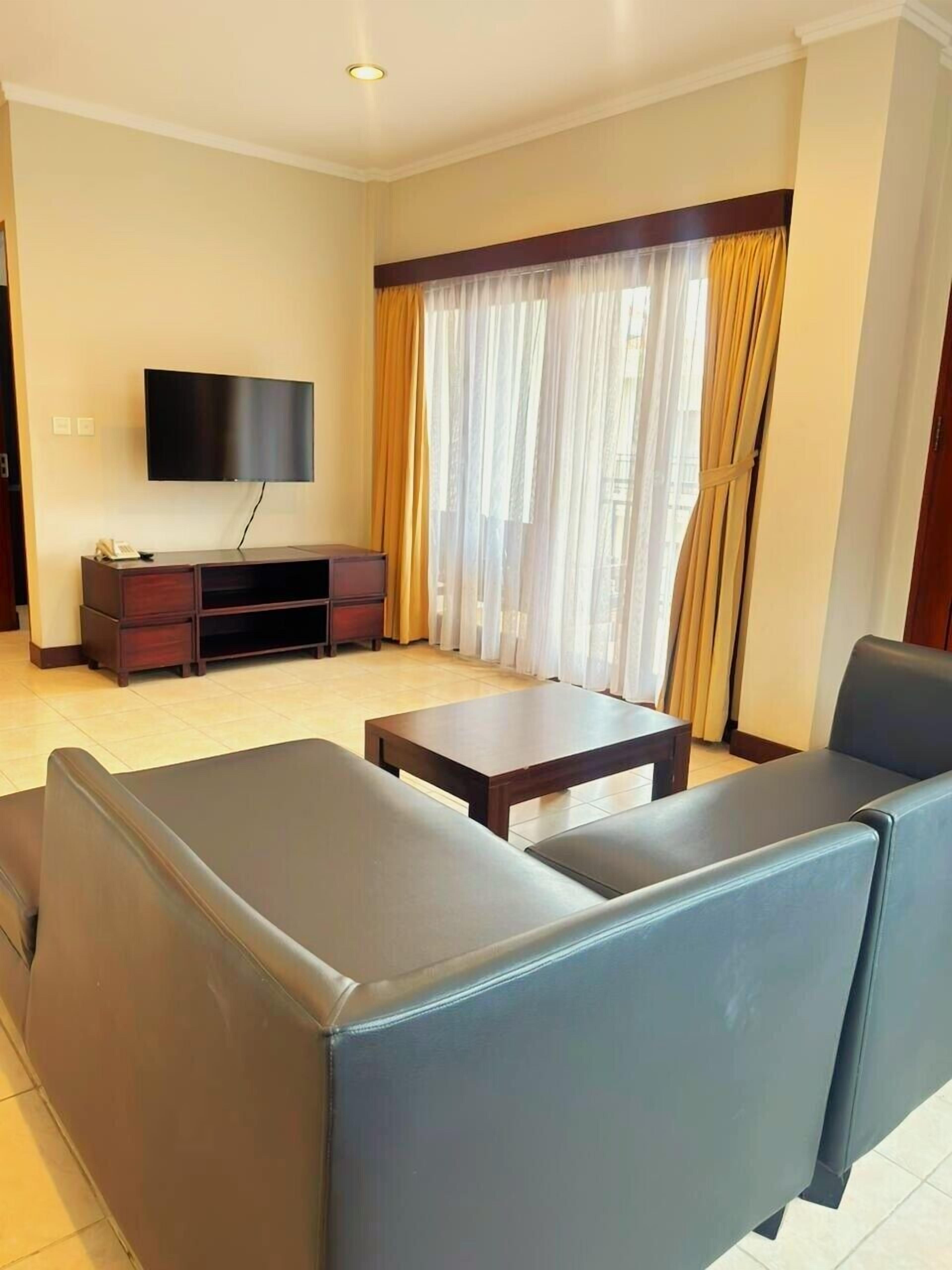 A living room with a flat-screen TV, a dark wooden coffee table, and two dark sofas.