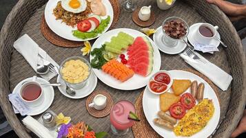 A tray with various breakfast items including eggs, toast, fruit, and beverages, placed on a woven mat near a pool.