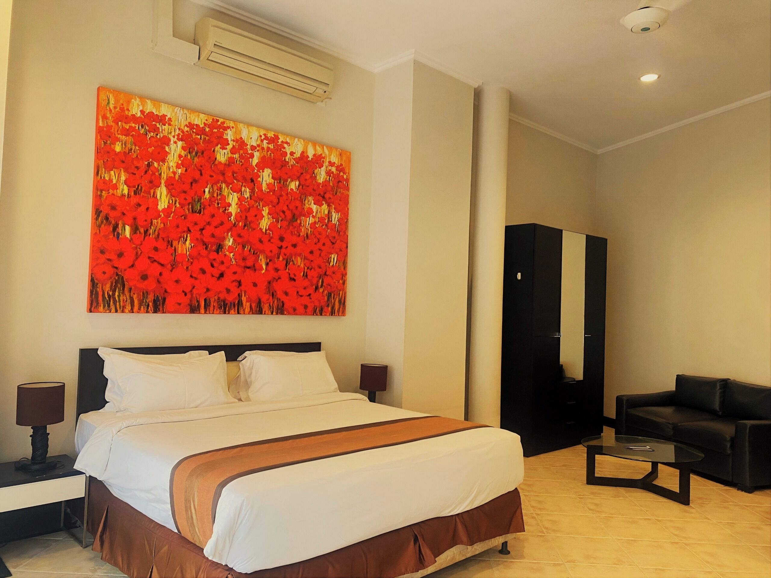 A hotel room with a large bed, a nightstand, a desk, a chair, a coffee table, and a painting on the wall.
