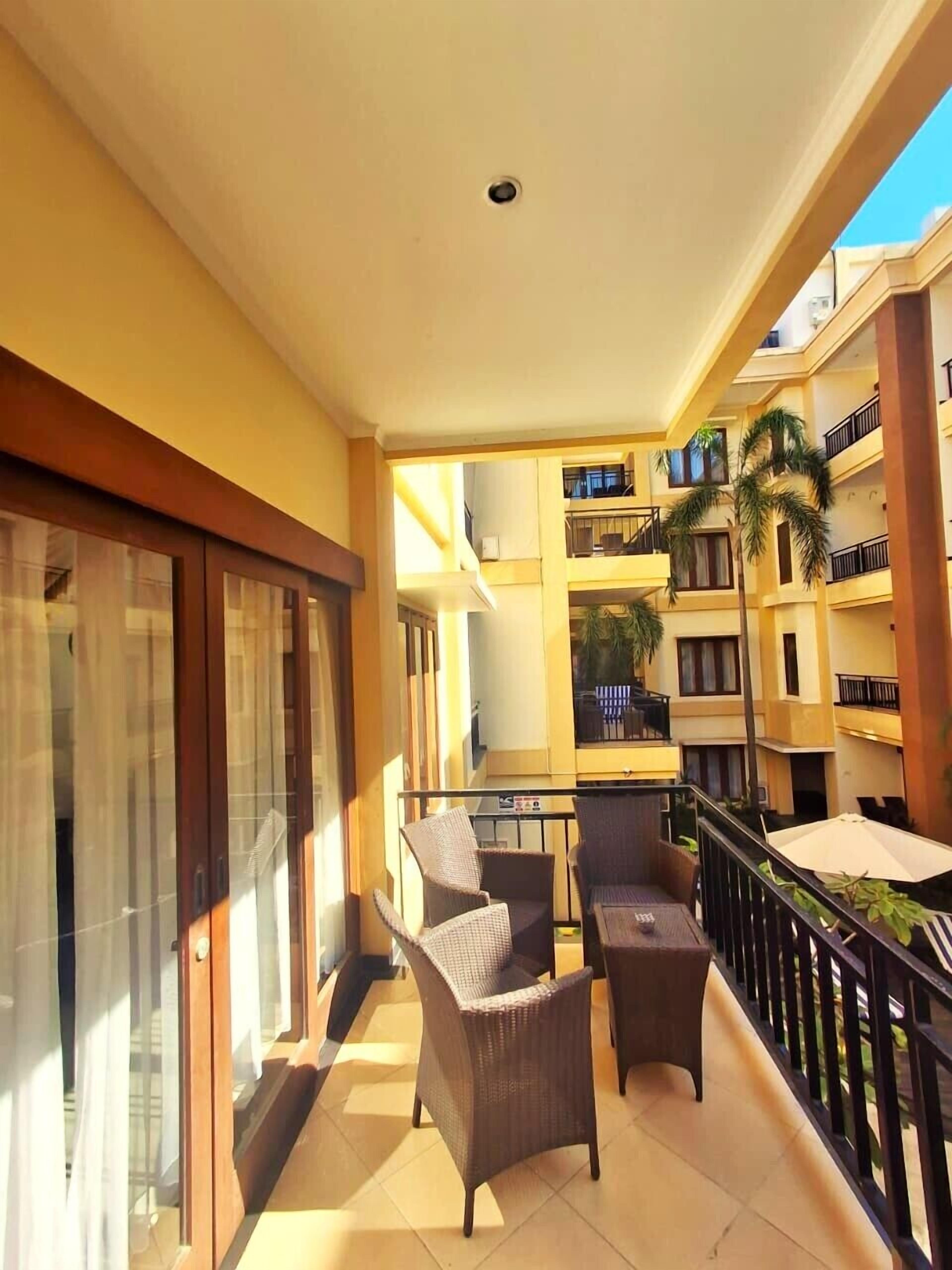 A balcony with wicker furniture, a glass door, and a view of a multi-story building with balconies.