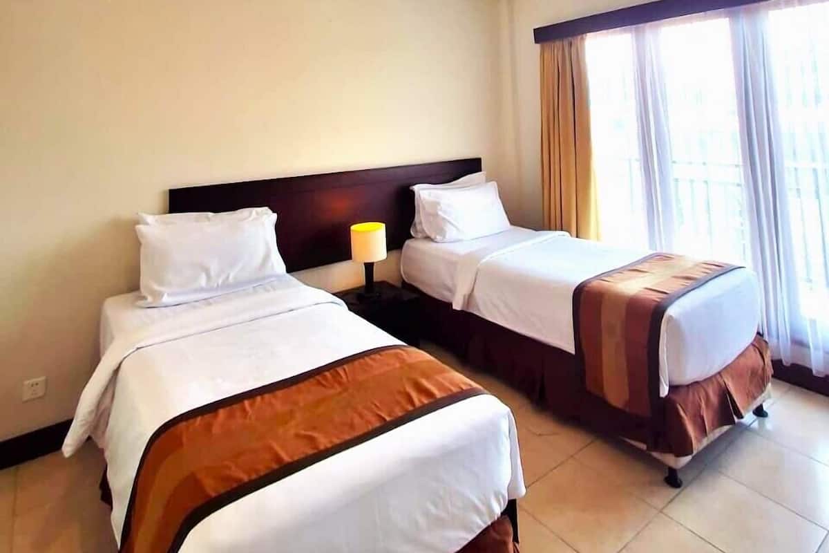 A hotel room with two beds, a ceiling fan, and a window with curtains.