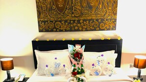 A hotel room with a bed, two bedside tables, a nightstand, a decorative wall tapestry, and a bouquet of flowers. - Kuta Townhouse Apartments (Kuta)