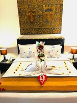 Una habitación de hotel con una cama, dos mesitas de noche, un florero y un tapiz decorativo en la pared.