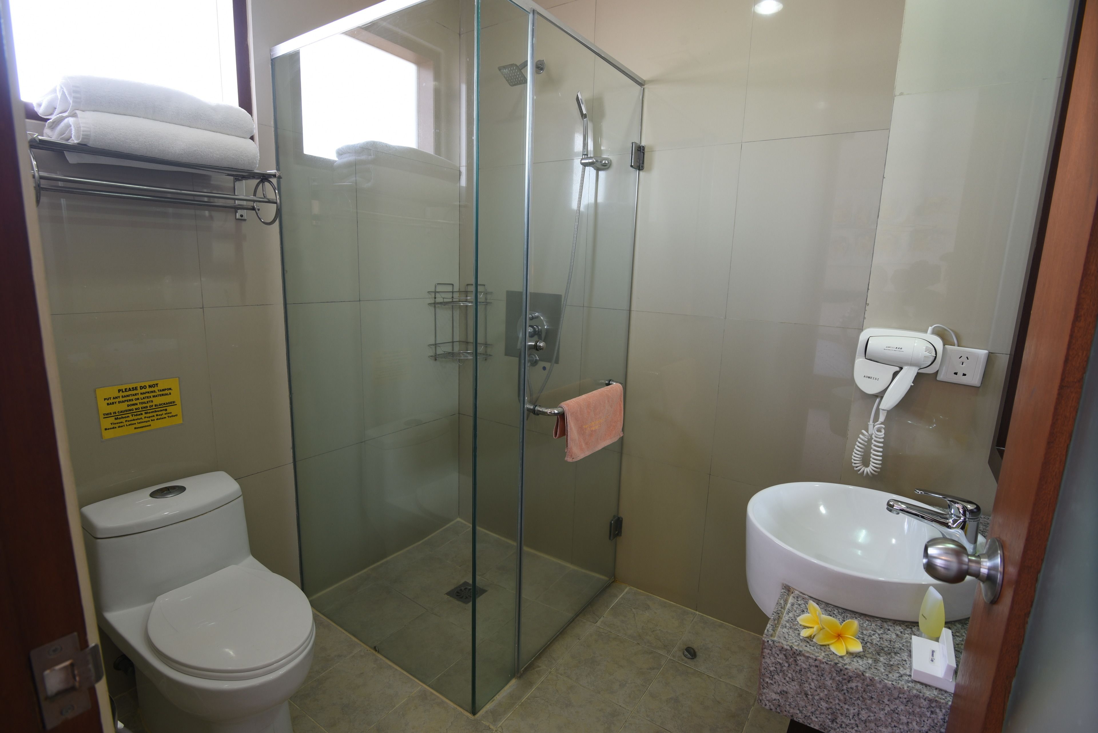 A bathroom with a glass-enclosed shower, a toilet, and a sink with a towel and flower on the counter.