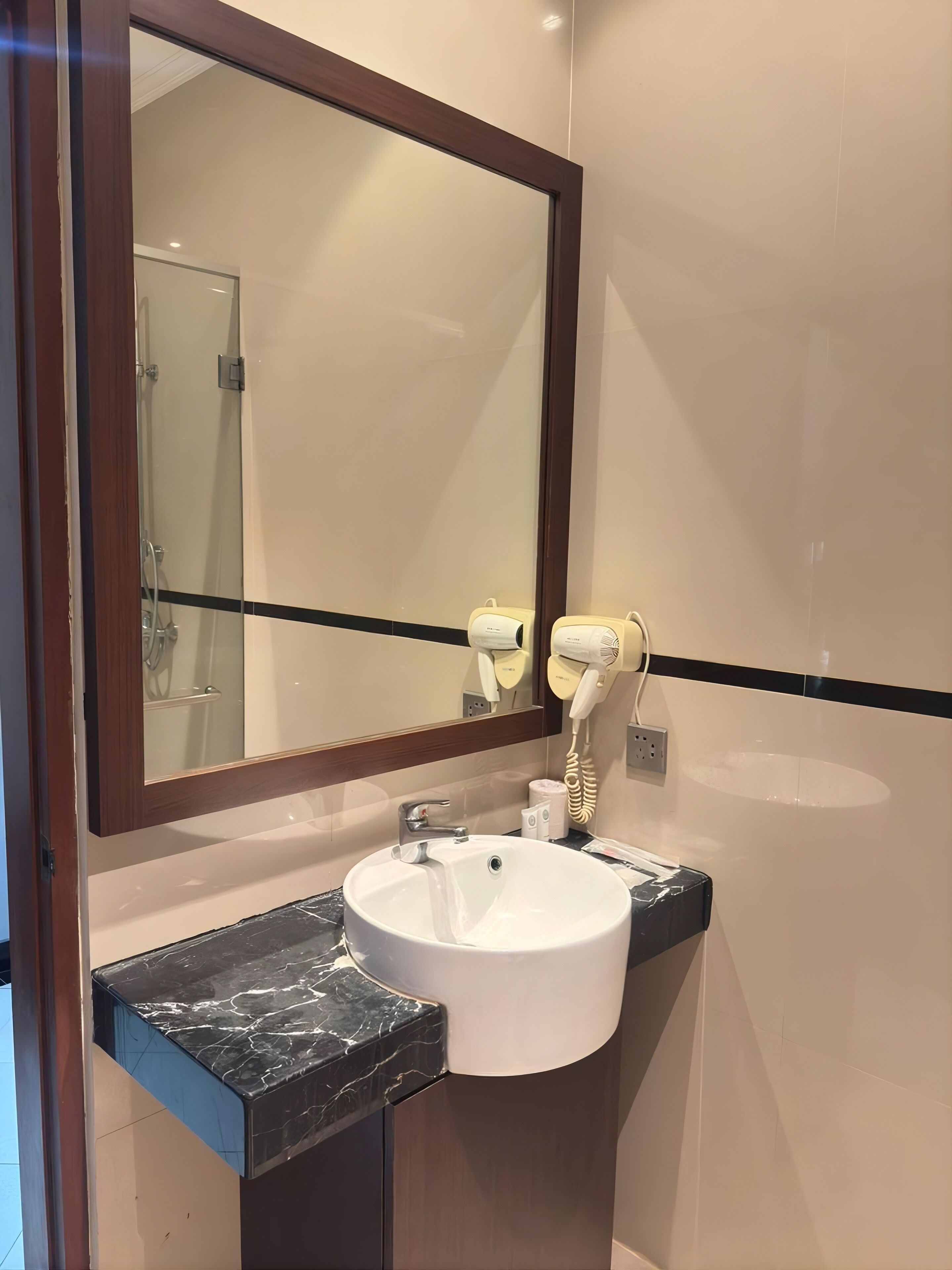 A bathroom with a large mirror, a white sink, a hairdryer, and a towel dispenser.