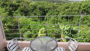 A balcony with a glass table and two chairs, overlooking a lush green landscape with hills in the distance. - Hibis Resort (Nakijin)