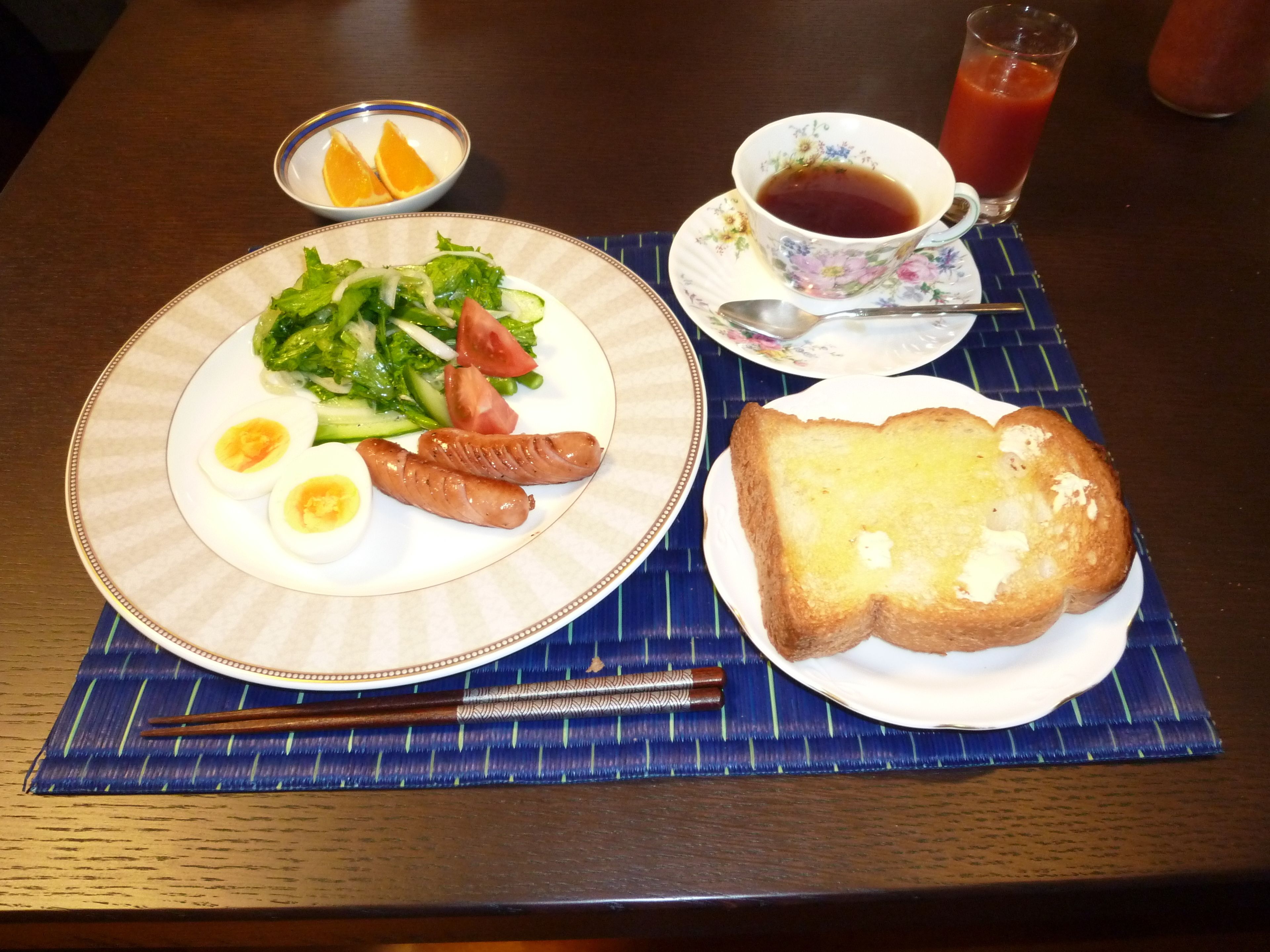 A plate with eggs, sausages, and salad, a slice of toast, a cup of tea, and a glass of juice on a table.