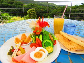 A meal on a blue-tiled table with a scenic view of green hills in the background. - Hibis Resort (Nakijin)