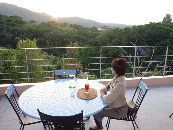 A person seated at a round table with a view of a forested landscape. - Hibis Resort (Nakijin)