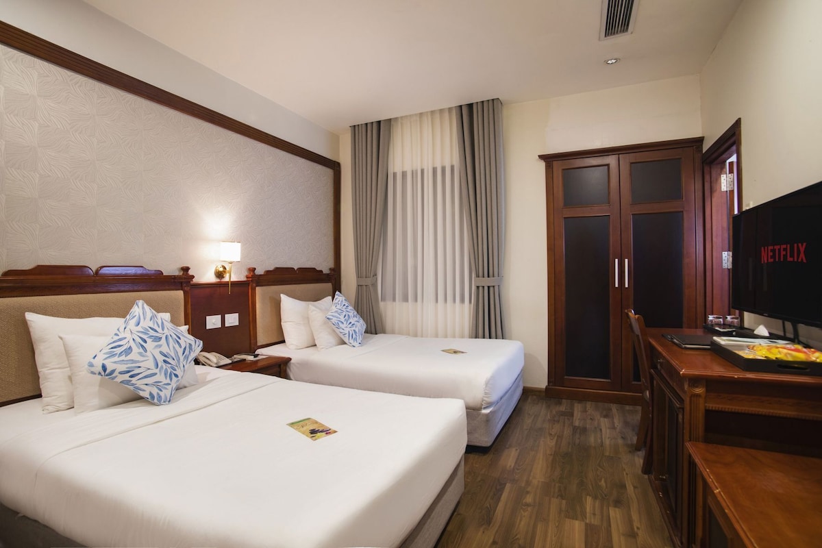 A hotel room with two beds, a TV, a desk, and a wardrobe.