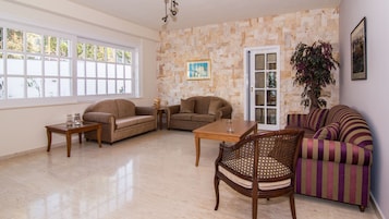 Un salón amplio con pared de piedra, una mesa de centro de madera, dos sofás, un sillón a rayas y una puerta que da al exterior.