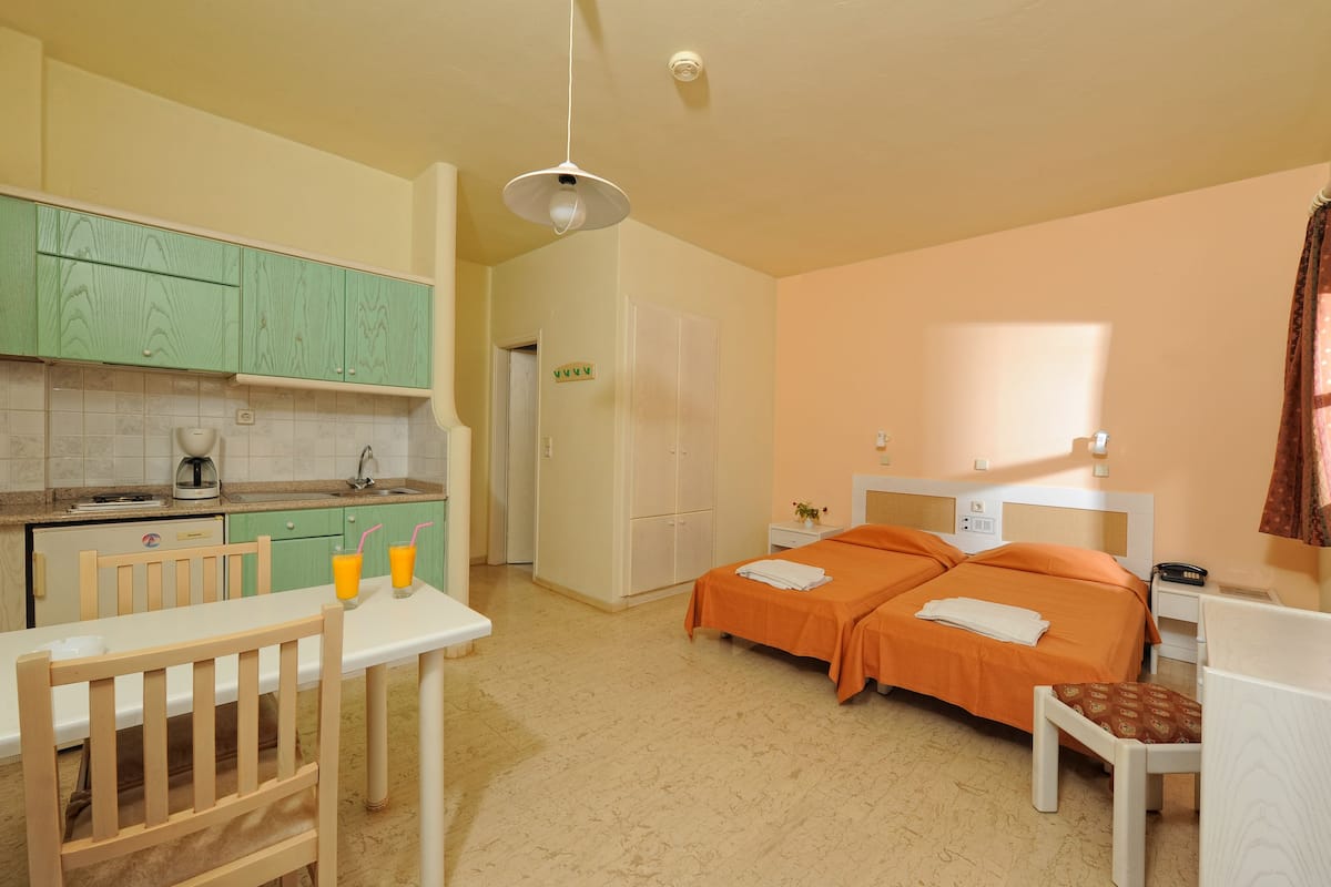 A compact room with a kitchenette, two beds, a dining table, and a small seating area.