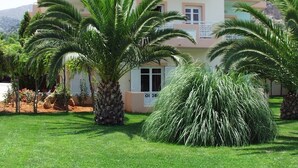 A multi-story building with balconies, surrounded by well-maintained grass and palm trees. - Manolis Apartments (Hersonissos)