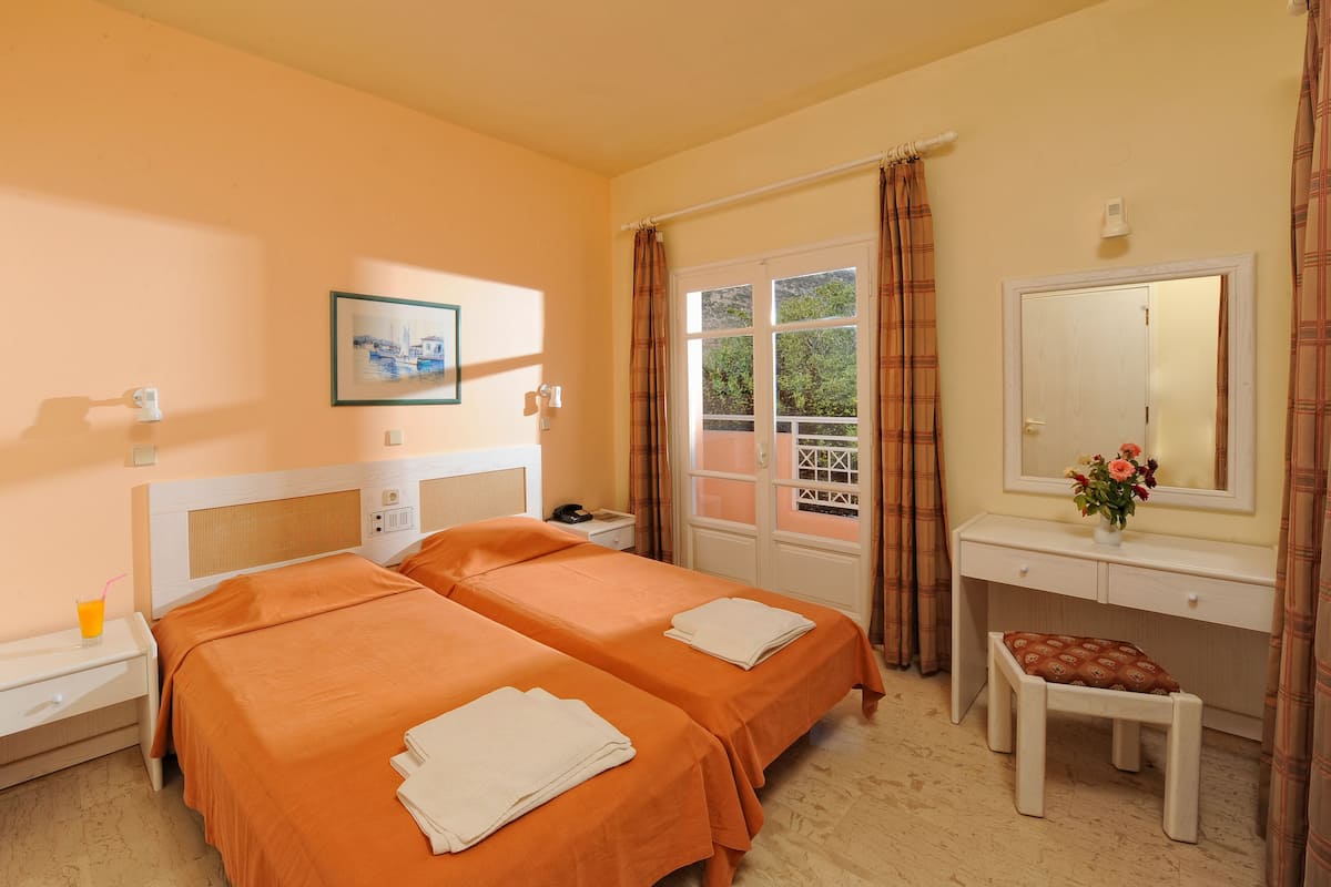 A hotel room with two beds, a desk, a chair, a nightstand, and a window with curtains.