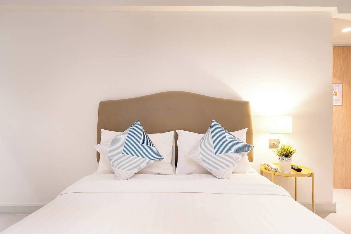 A neatly made bed with a headboard, two bedside tables with lamps, and a small potted plant.