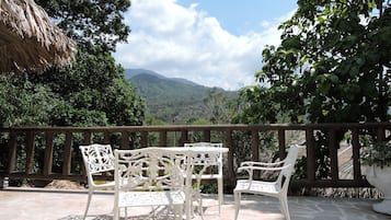 A terrace with white wrought iron chairs and a table, overlooking a mountainous landscape.