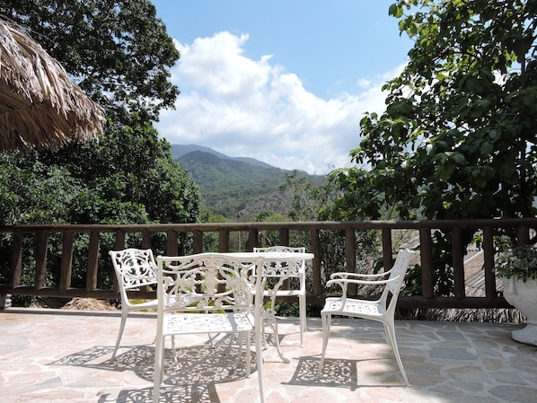 A terrace with white wrought iron chairs and a table, overlooking a mountainous landscape.
