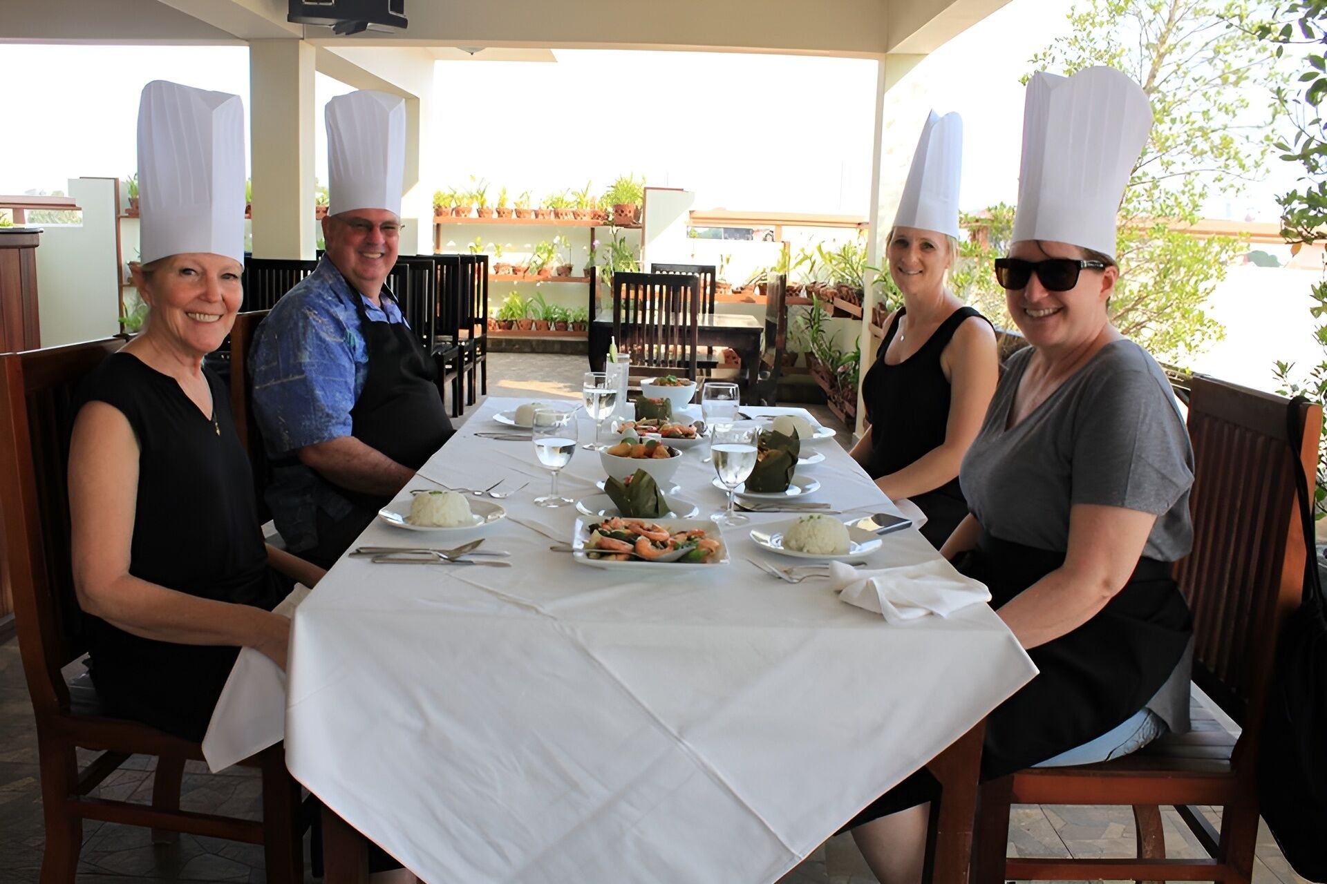 A group of people seated at a table with a white tablecloth, plates of food, and a variety of dishes.