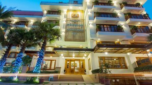 Un hotel de varios pisos con una entrada destacada, balcones con plantas y una fachada bien iluminada.