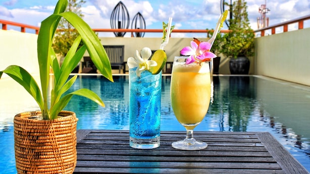 Escena junto a la piscina con una planta de mimbre, una bebida azul con una rodaja de lima y una bebida amarilla con pajita.
