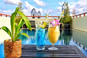 A poolside setting with a wicker plant, a blue drink with a lime slice, and a yellow drink with a straw. - Cheathata CTS Hotel Siem Reap (Siem Reap)