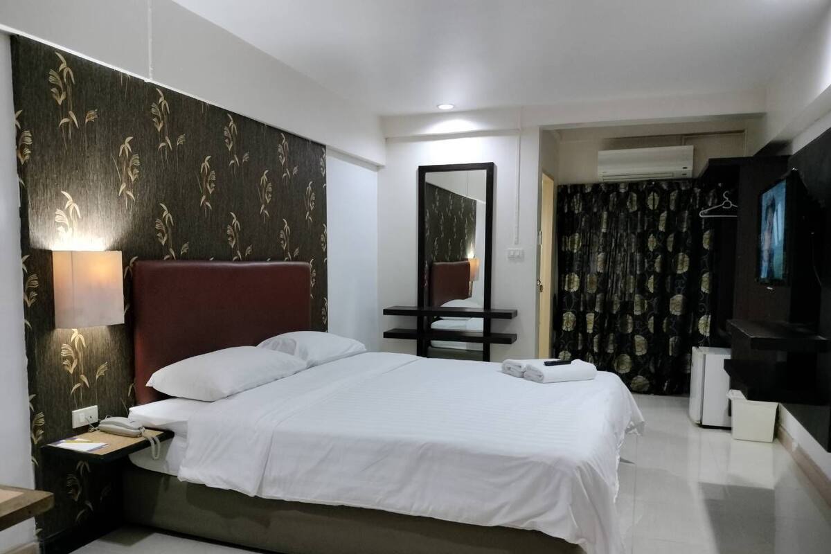 Een hotelkamer met een groot bed, een nachtkastje met een lamp, een spiegel, een televisie en een kledingkast.