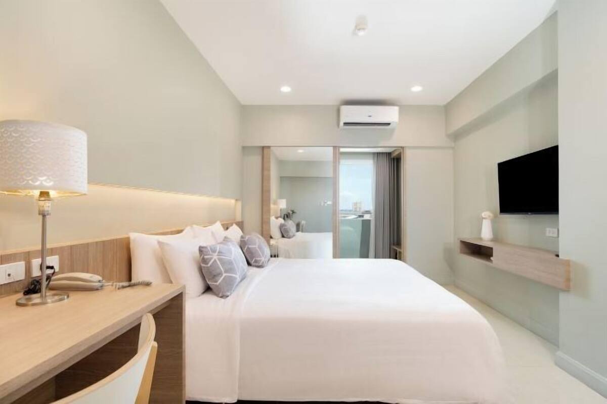 Een moderne hotelkamer met een bed, bureau en een aan de muur bevestigde televisie.