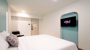 A hotel room with a bed, a TV mounted on the wall, a door, and a light fixture.