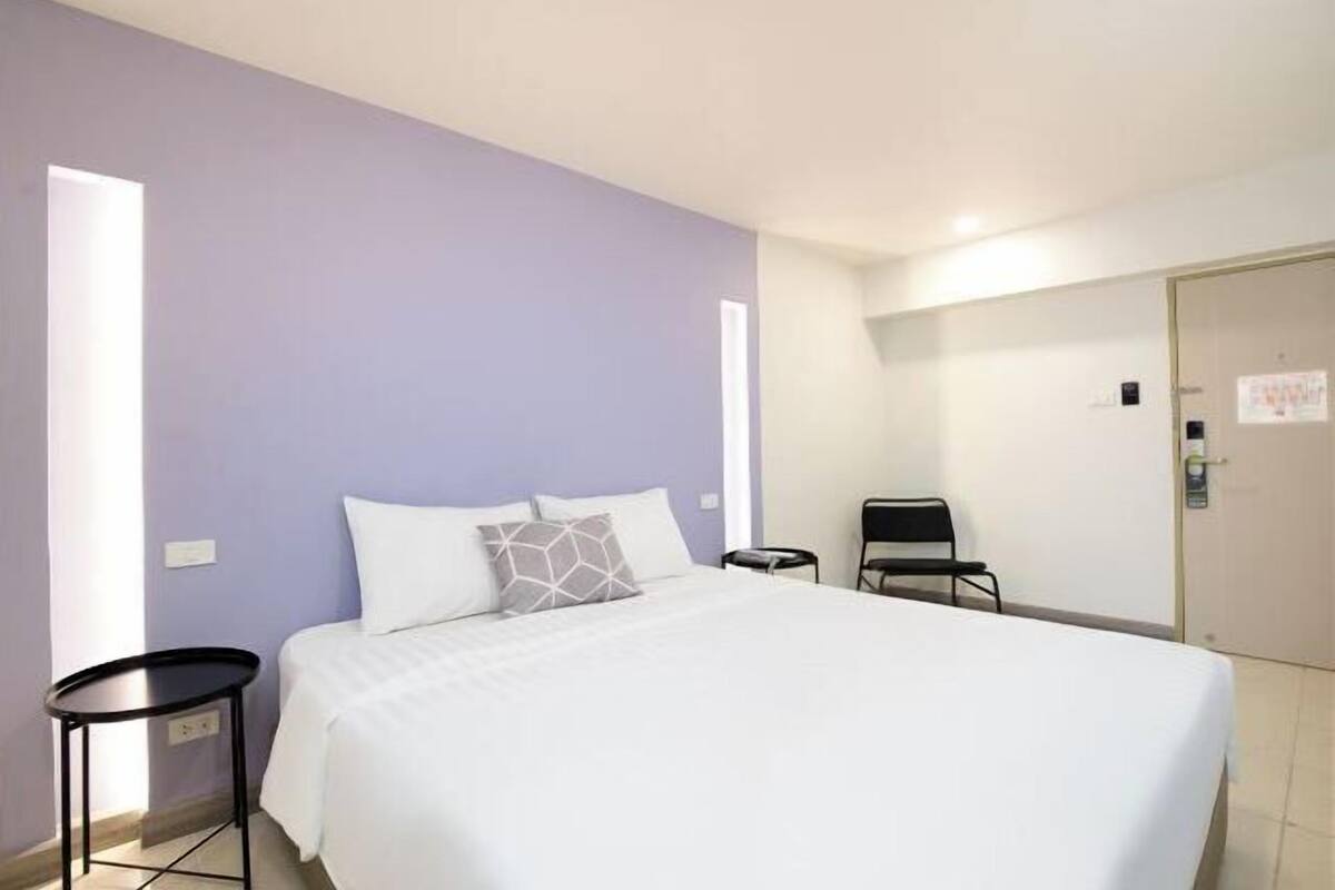 Een hotelkamer met een bed, een klein tafeltje, een stoel en een deur.