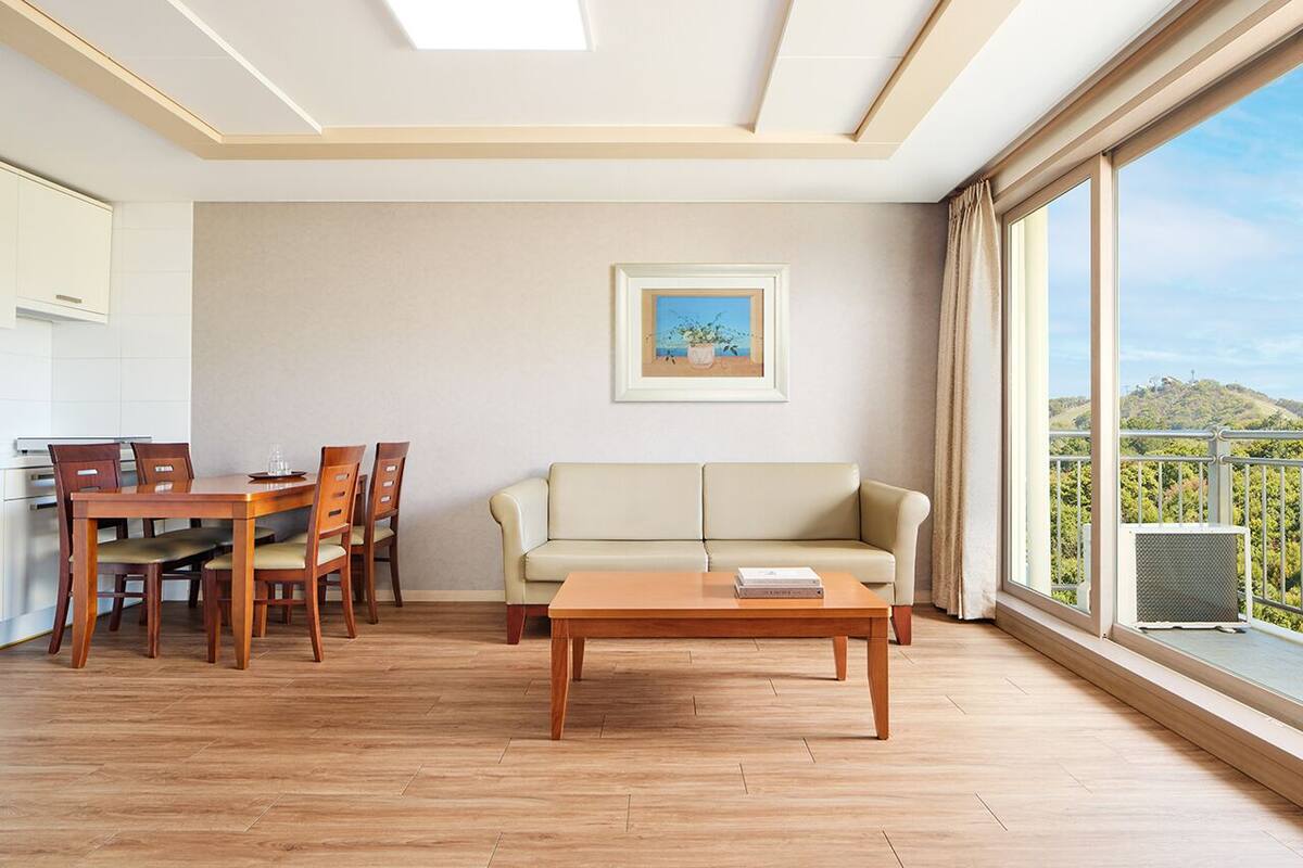 Un salon moderne avec une table à manger en bois, un canapé beige et une grande fenêtre donnant sur un balcon.