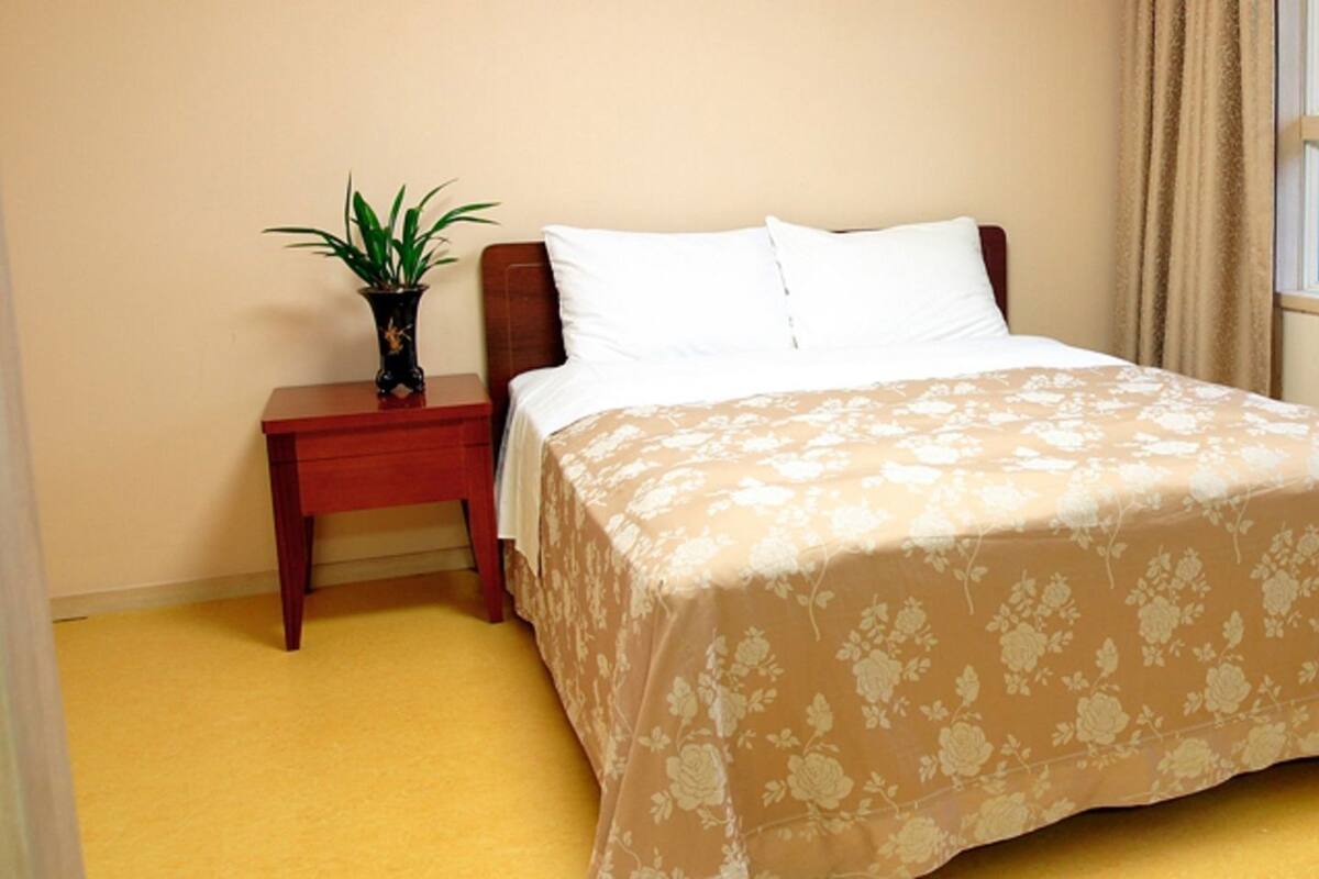 Une chambre à coucher avec un lit, une table de chevet, une plante en pot et une fenêtre donnant sur un beau paysage.