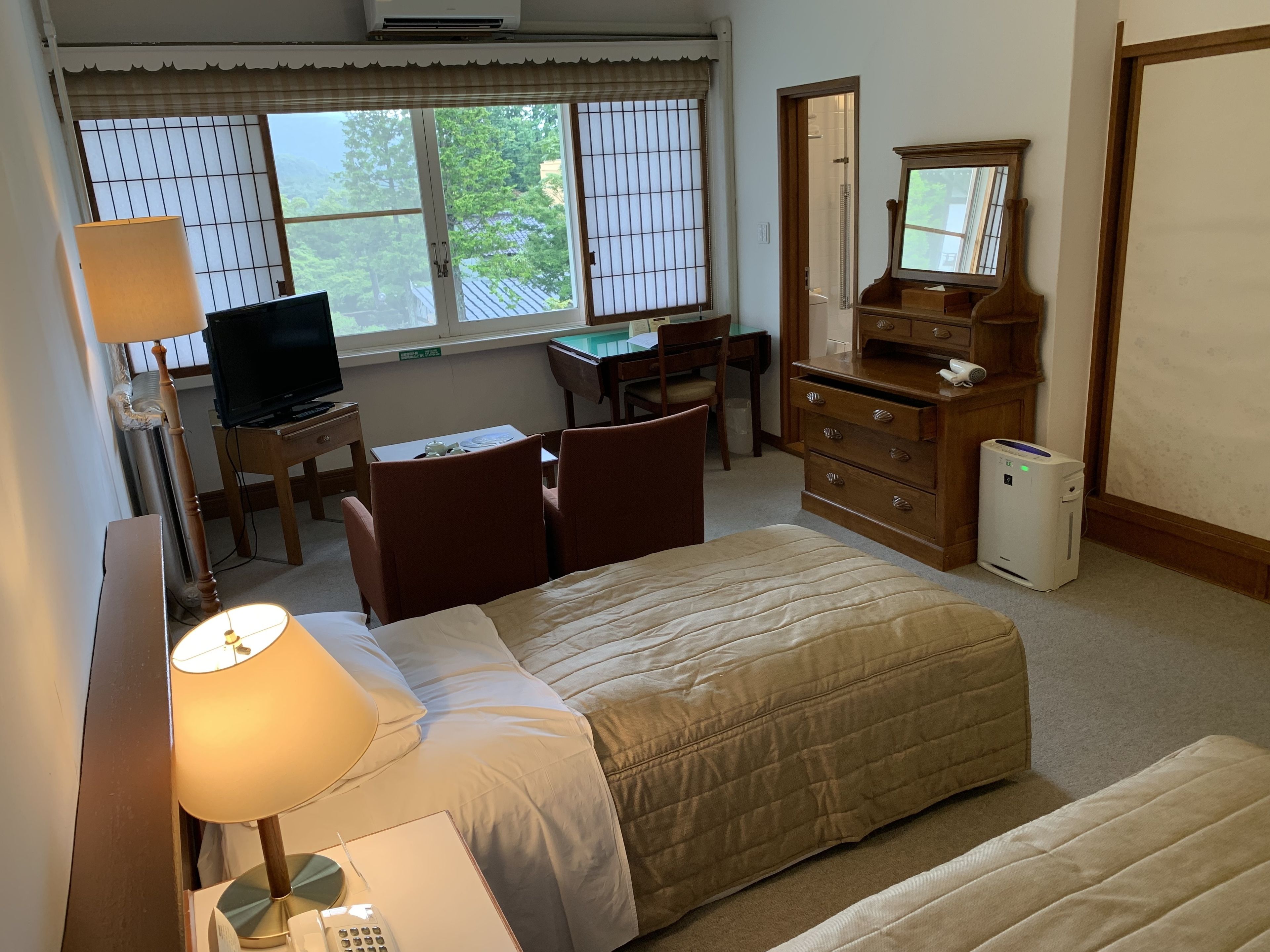 A hotel room with a bed, desk, chair, dresser, and a television.