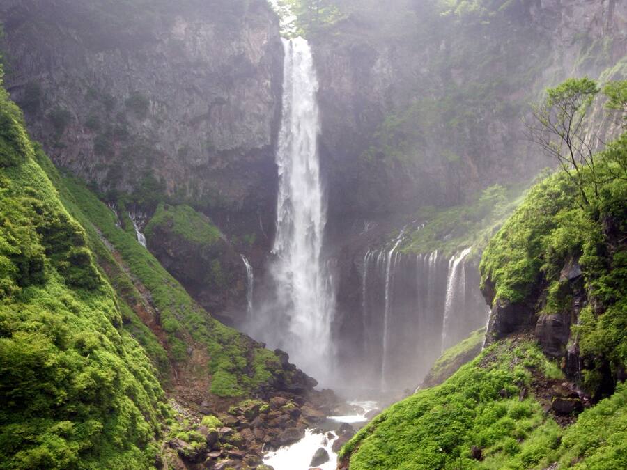 Uma cascata despenca por um penhasco íngreme e rochoso, cercada por vegetação exuberante.