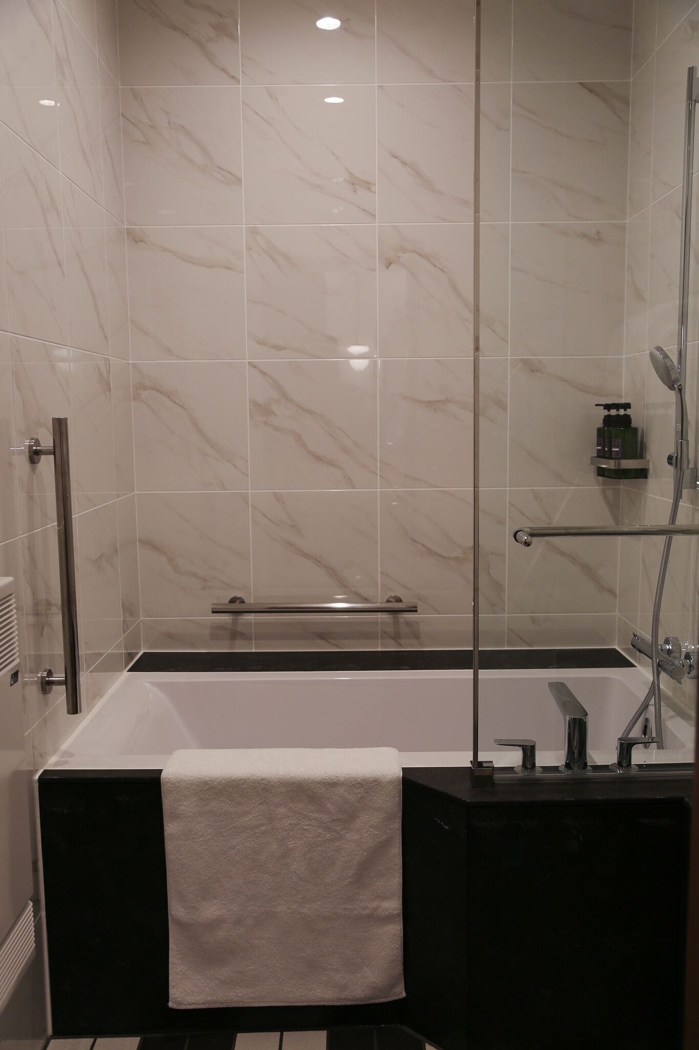 Un baño moderno con ducha de vidrio, una bañera negra y una toalla blanca en el borde.