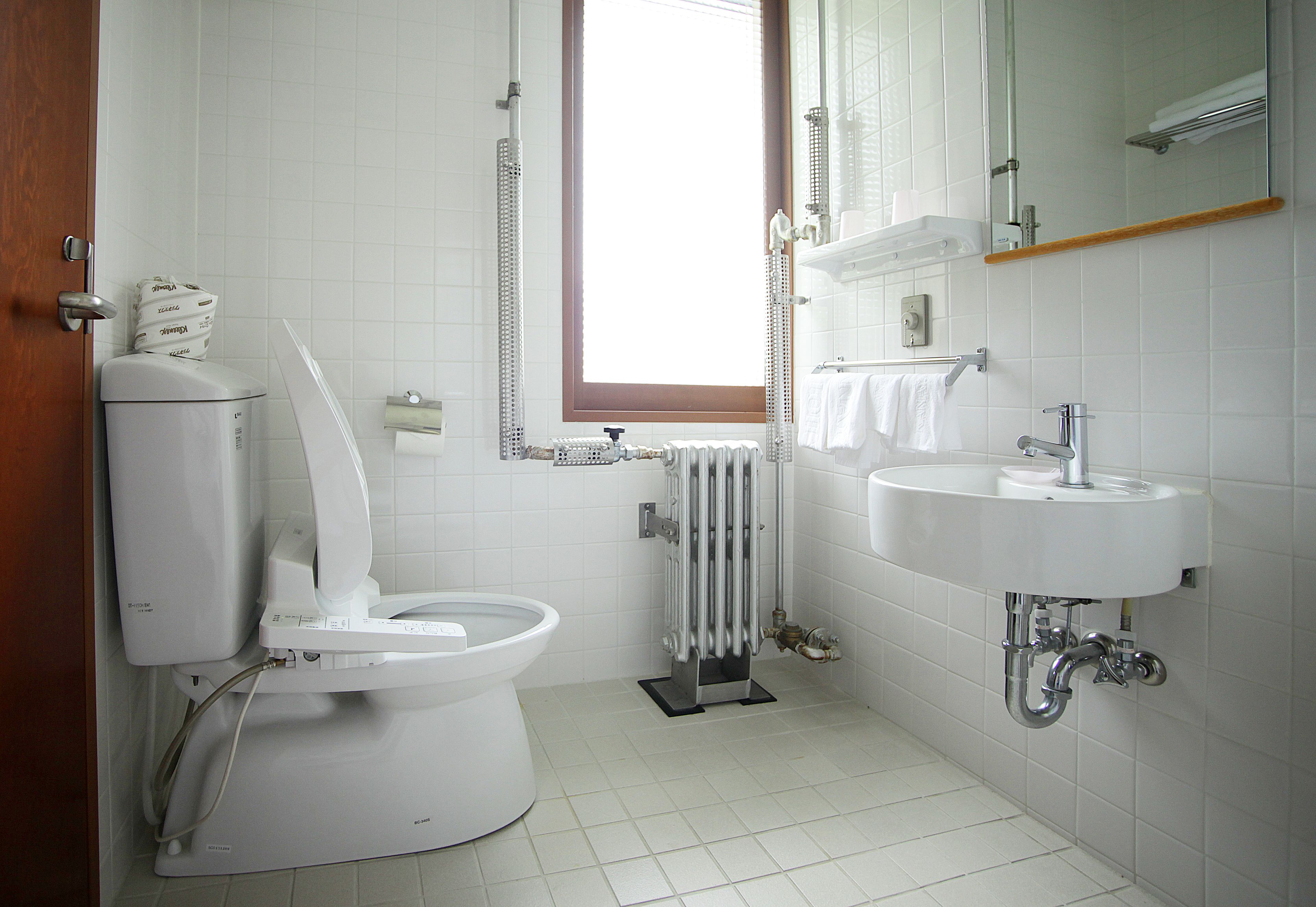 A modern bathroom with a toilet, bidet, radiator, sink, and a window providing natural light.