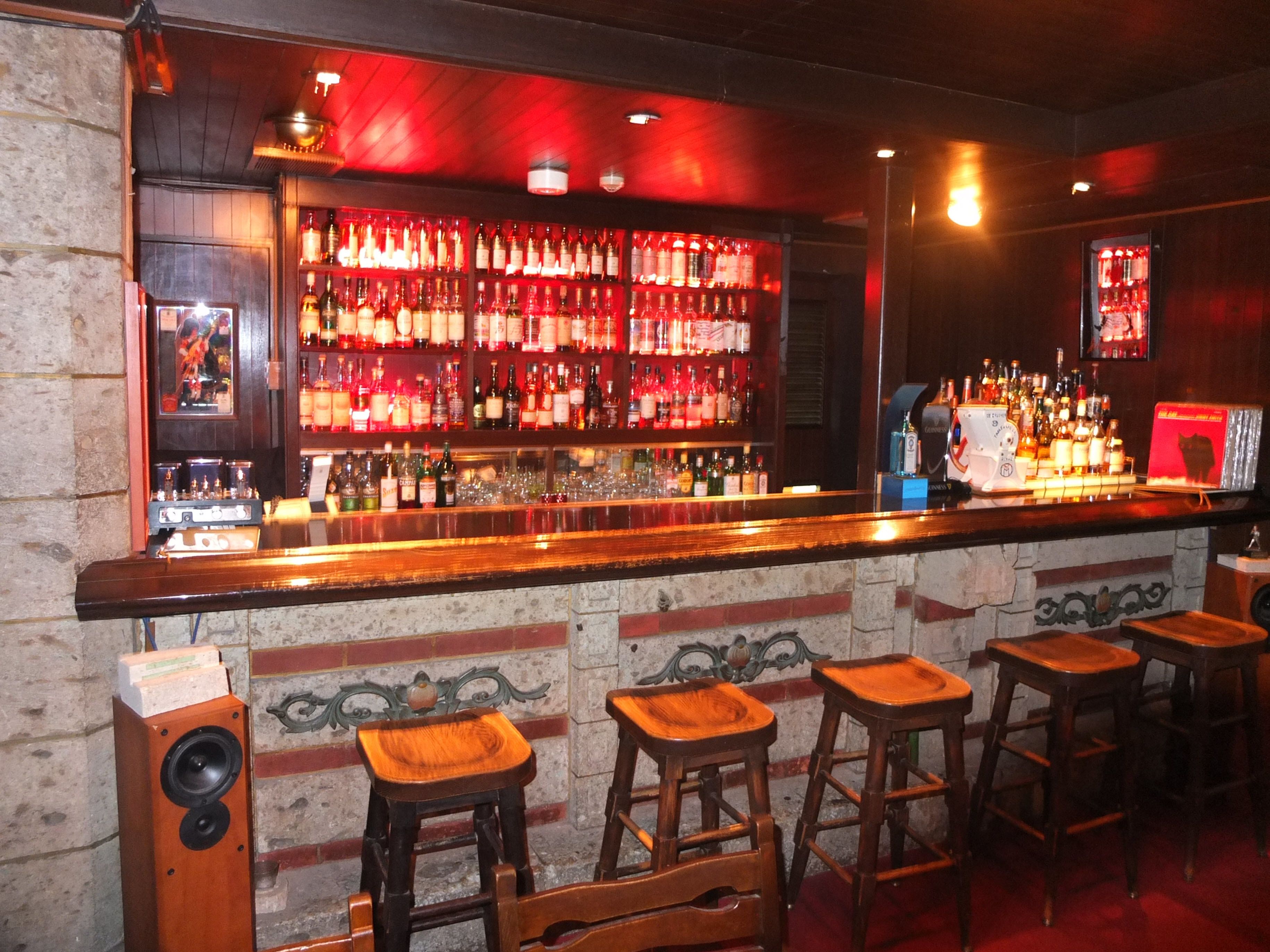 Een bar met een houten toonbank, verschillende krukken en een wand vol drankflessen.