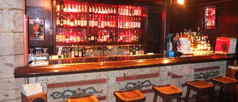 Een bar met een houten toonbank, verschillende krukken en een wand vol drankflessen.