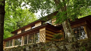 Un edificio de madera tradicional con ventanas amplias, rodeado de árboles y rocas.