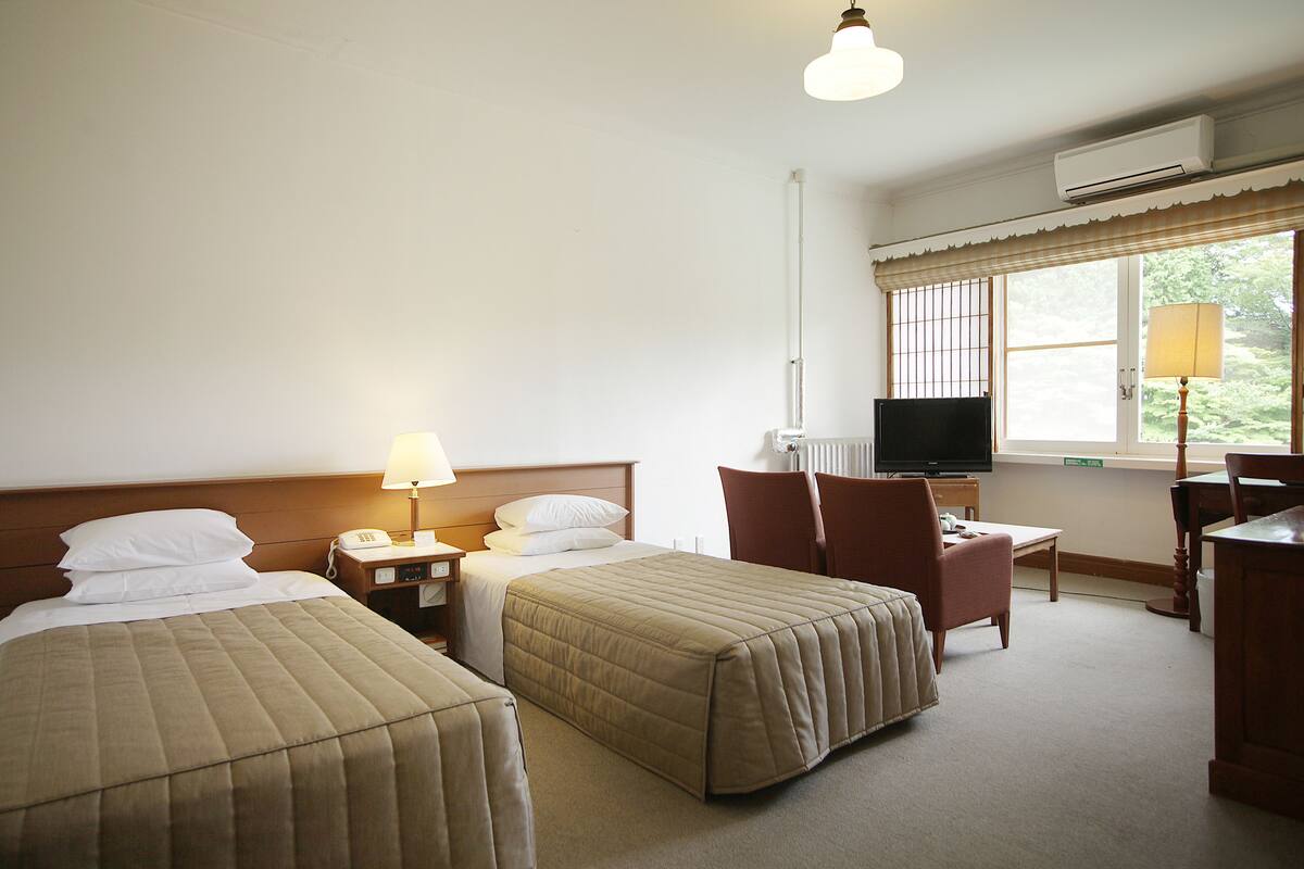 A hotel room with two beds, a desk, a chair, a television, and a window with a view.