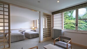 Habitación de hotel con dos camas, una mesa, una silla, un radiador y una ventana con vistas a zonas verdes.